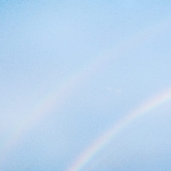 NEVER ENOUGH album cover — light rainbow on a blue sky